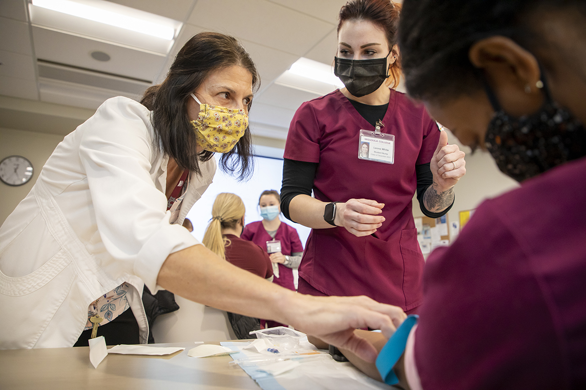 A female nurse in a white jacket teaching other nurses how to insert an IV