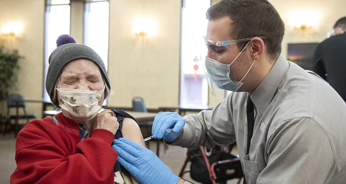 A UM pharmacy student gives the COVID-19 vaccine to an elderly woman. 