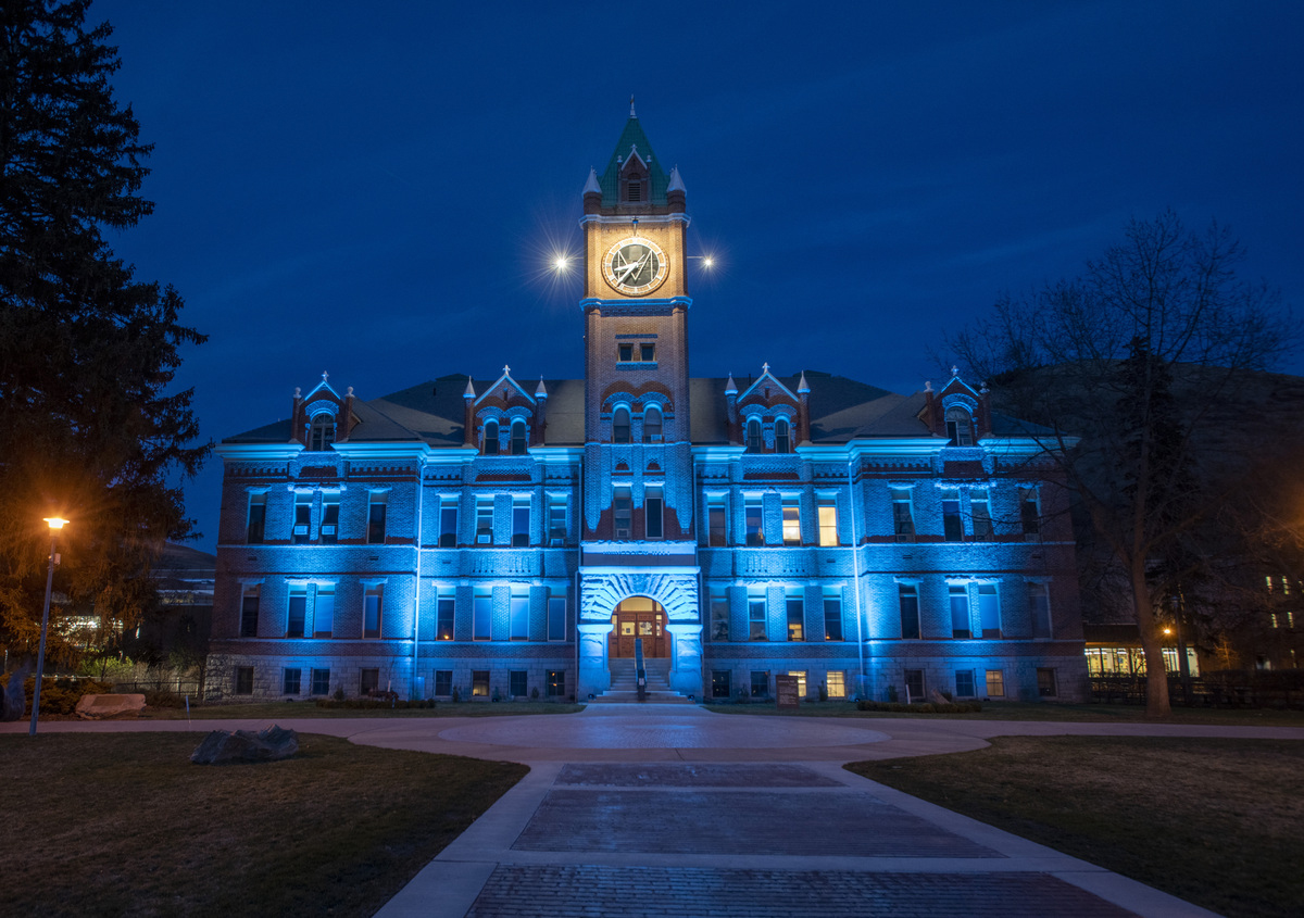 A view from the University of Montana Oval of Main Hall lit up in teal at night