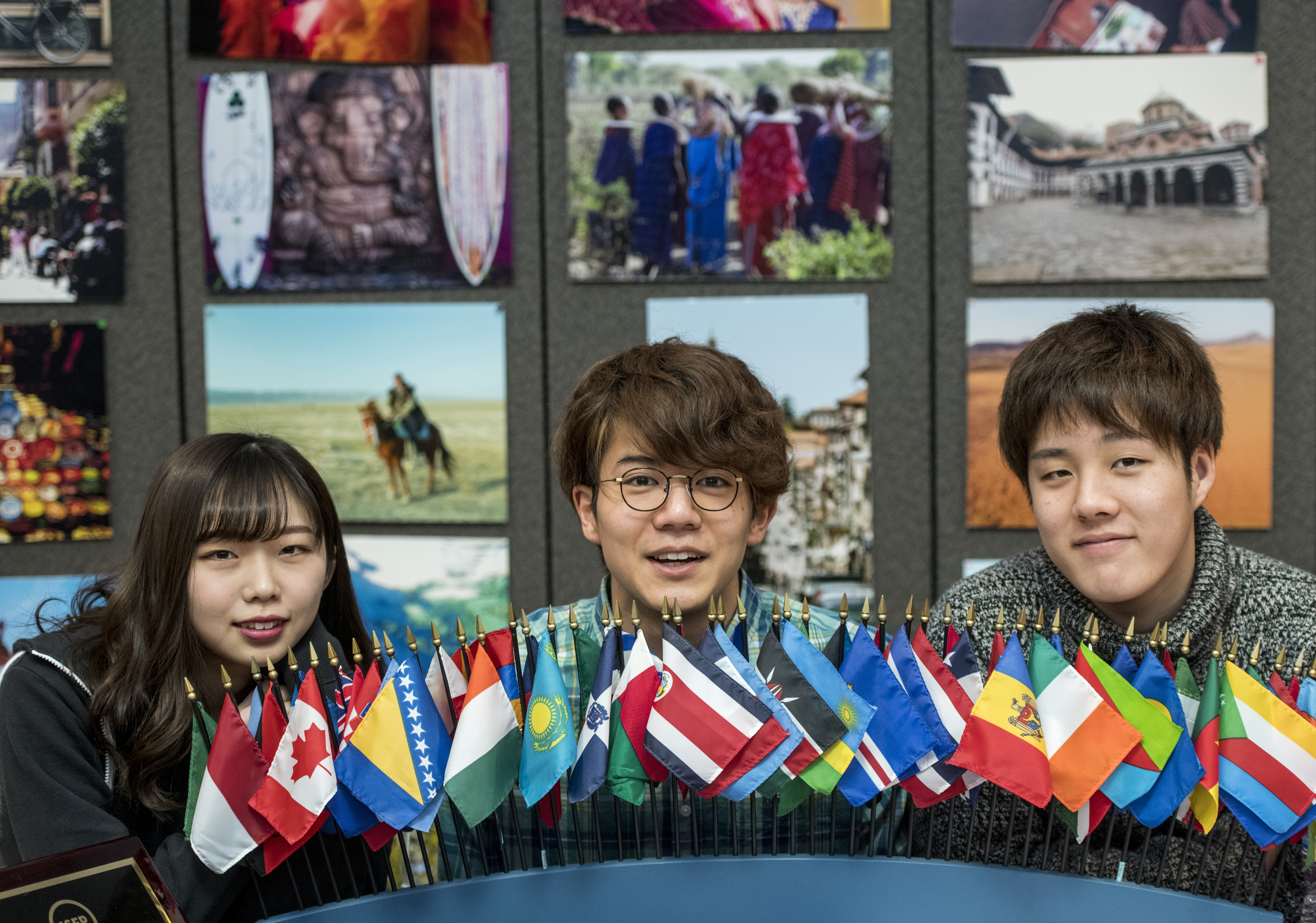 Three international students sit behind miniature flags from countries around the world.