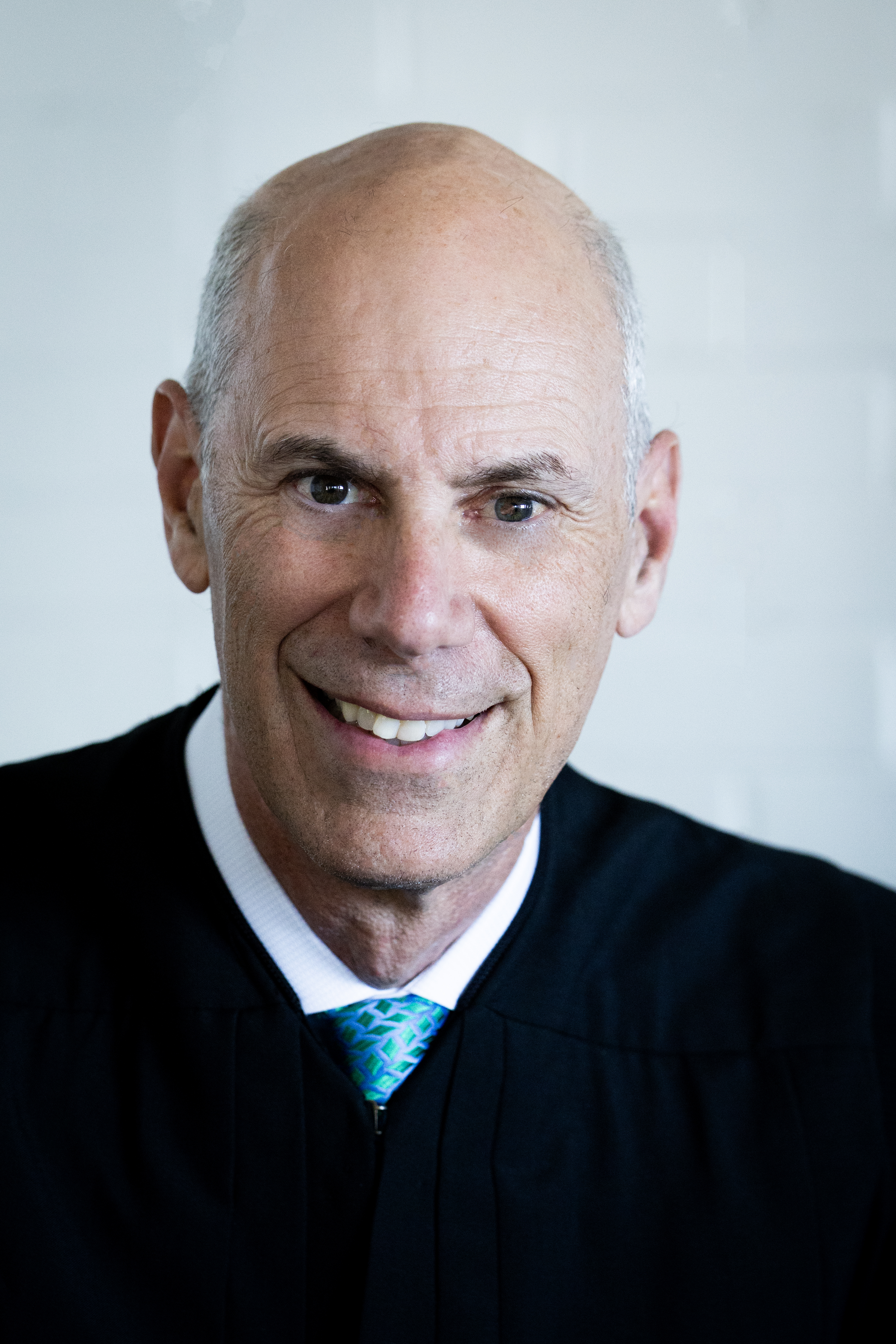 Close-up portrait of a smiling man wearing a black judicial robe and a blue-green patterned tie.