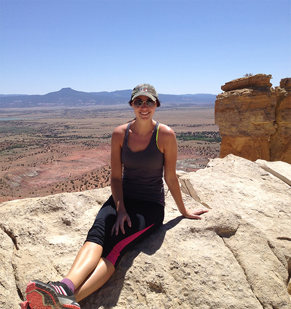 jordon Scotti sitting on a rocky ledge overlooking a wide desert valley and distant mountains on a sunny day.