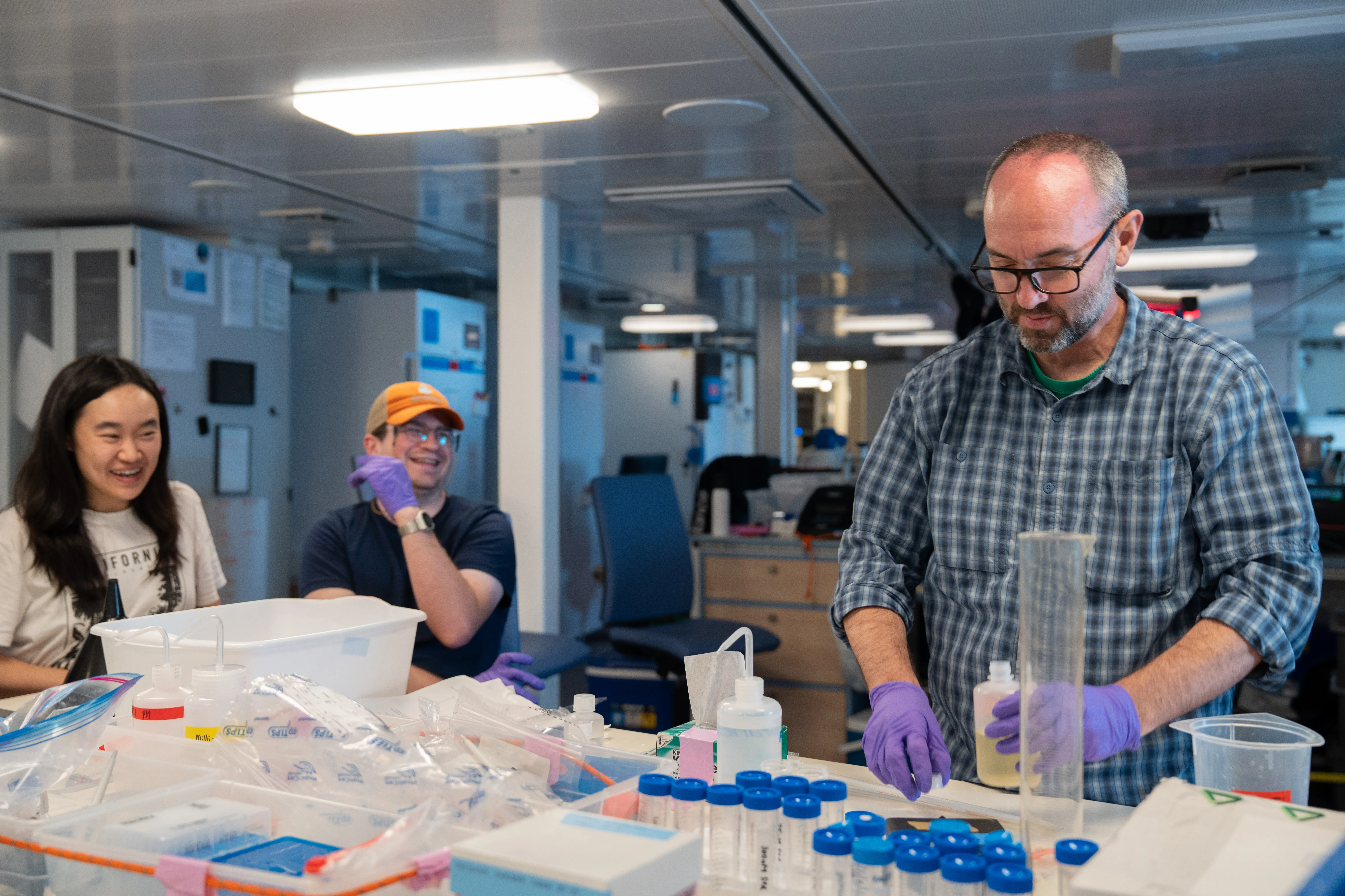 Matthew Church, Chief Scientist and Professor at UM shows seawater sample to Esther Wing Kwan Mak, Ocean Scientist and Postdoctoral Researcher at FLBS, UM and Jared McGourty, Systems Ecology Graduate Student, UM after pipetting to measure phosphate concentrations at the main lab aboard Falkor (too). CREDIT: Bernarda Cornejo Pinto / Schmidt Ocean Institute