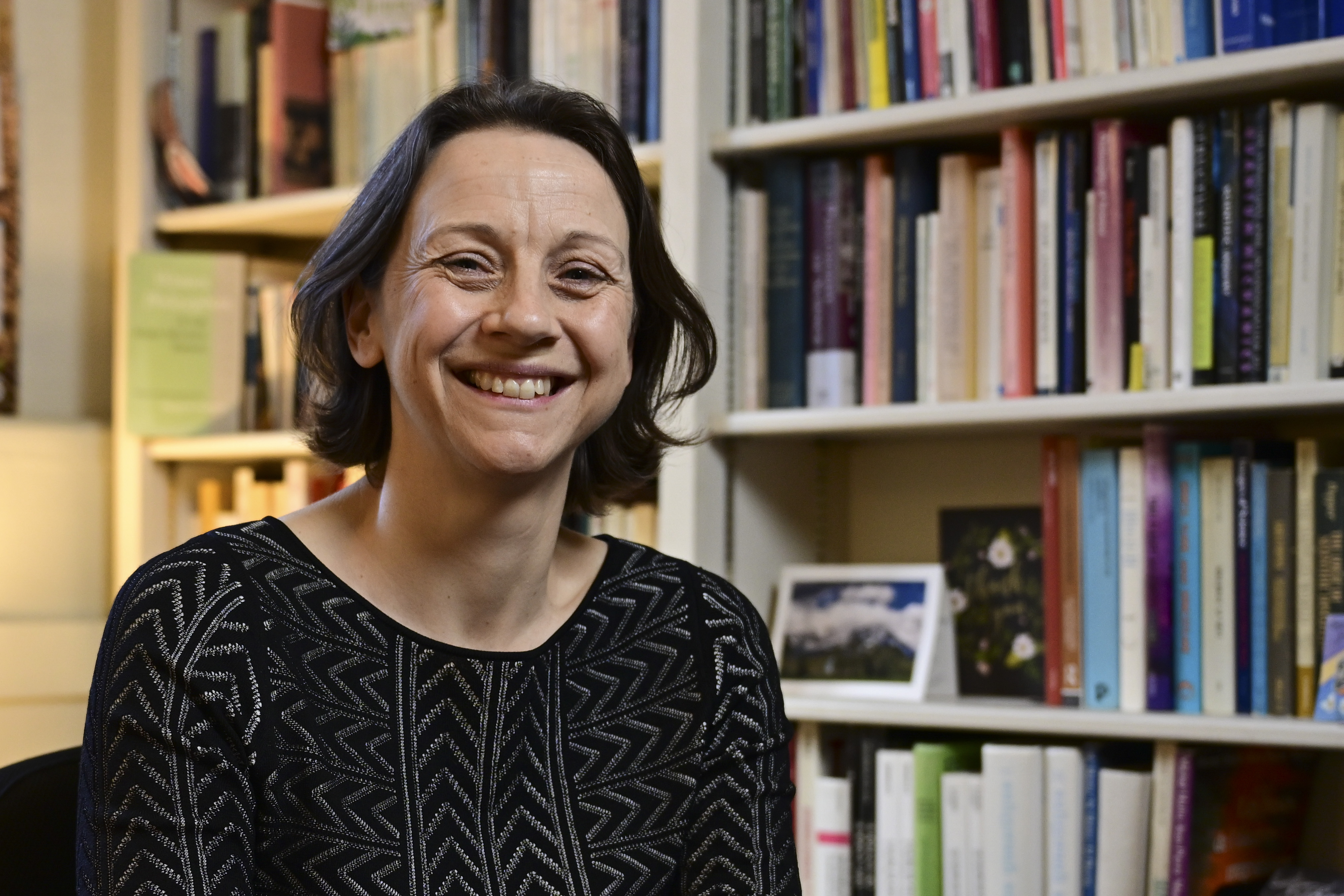Soazig sitting in front of a book shelf with a big smile