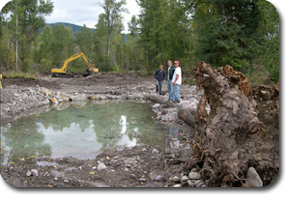 three men standing by excavation equiment and a hole filled with water