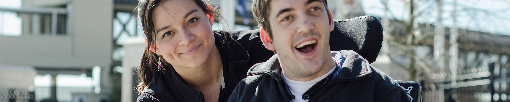 Woman and man with visible disabilites smile at the camera outside