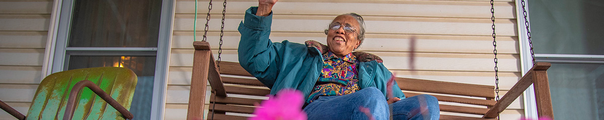      Woman sitting on a porch swing smiling and waving