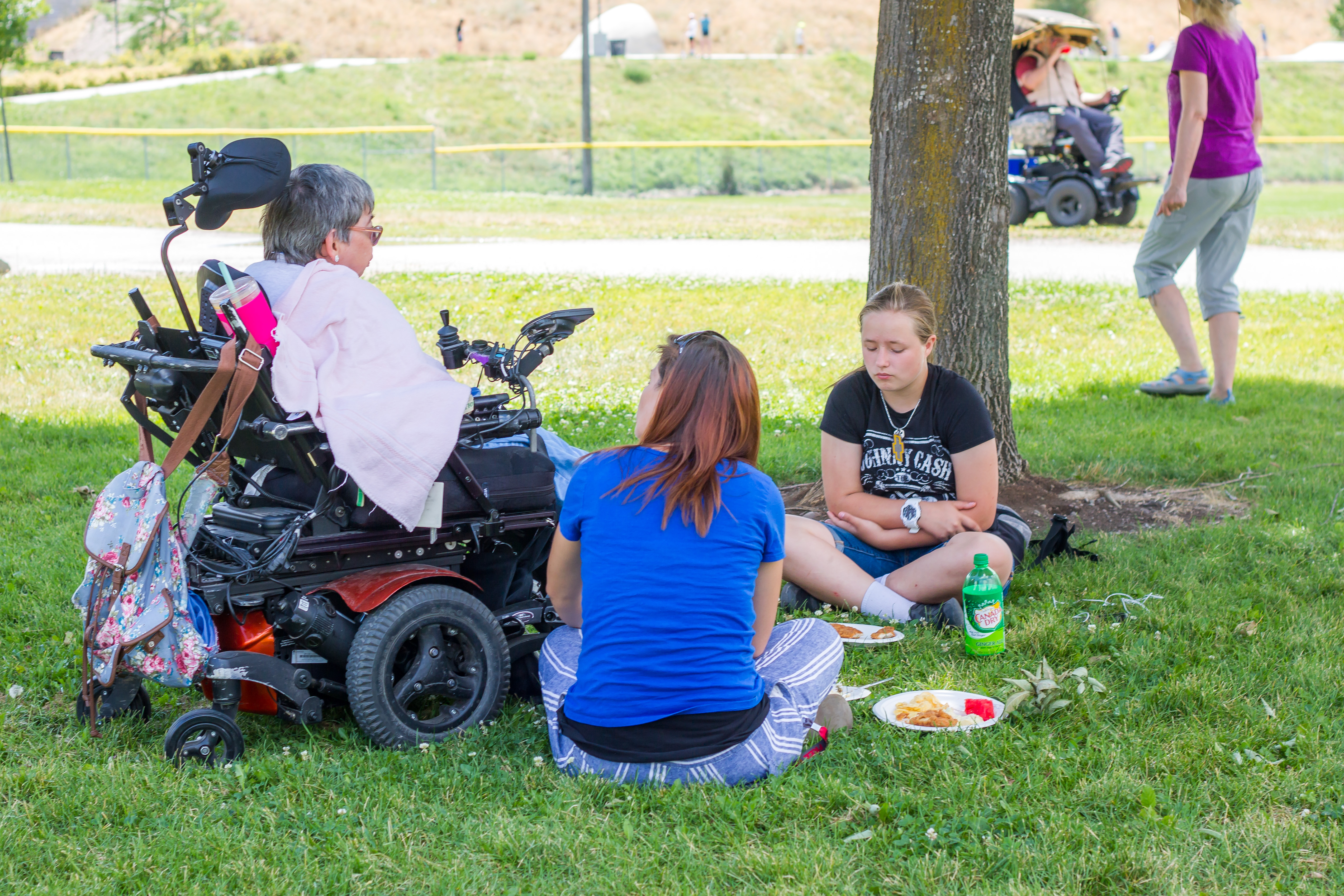 three people, one using a motorized wheelchair, at an outside picnic