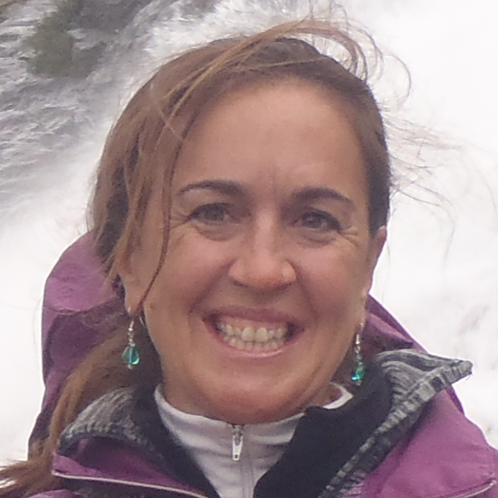 woman smiling at the camera, standing in front of a waterfall.