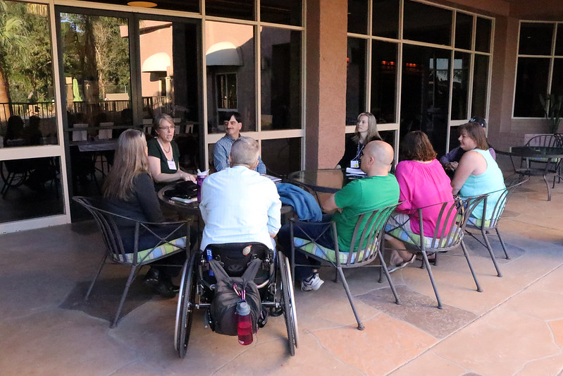 Many people including a person in a wheelchair around a table talking