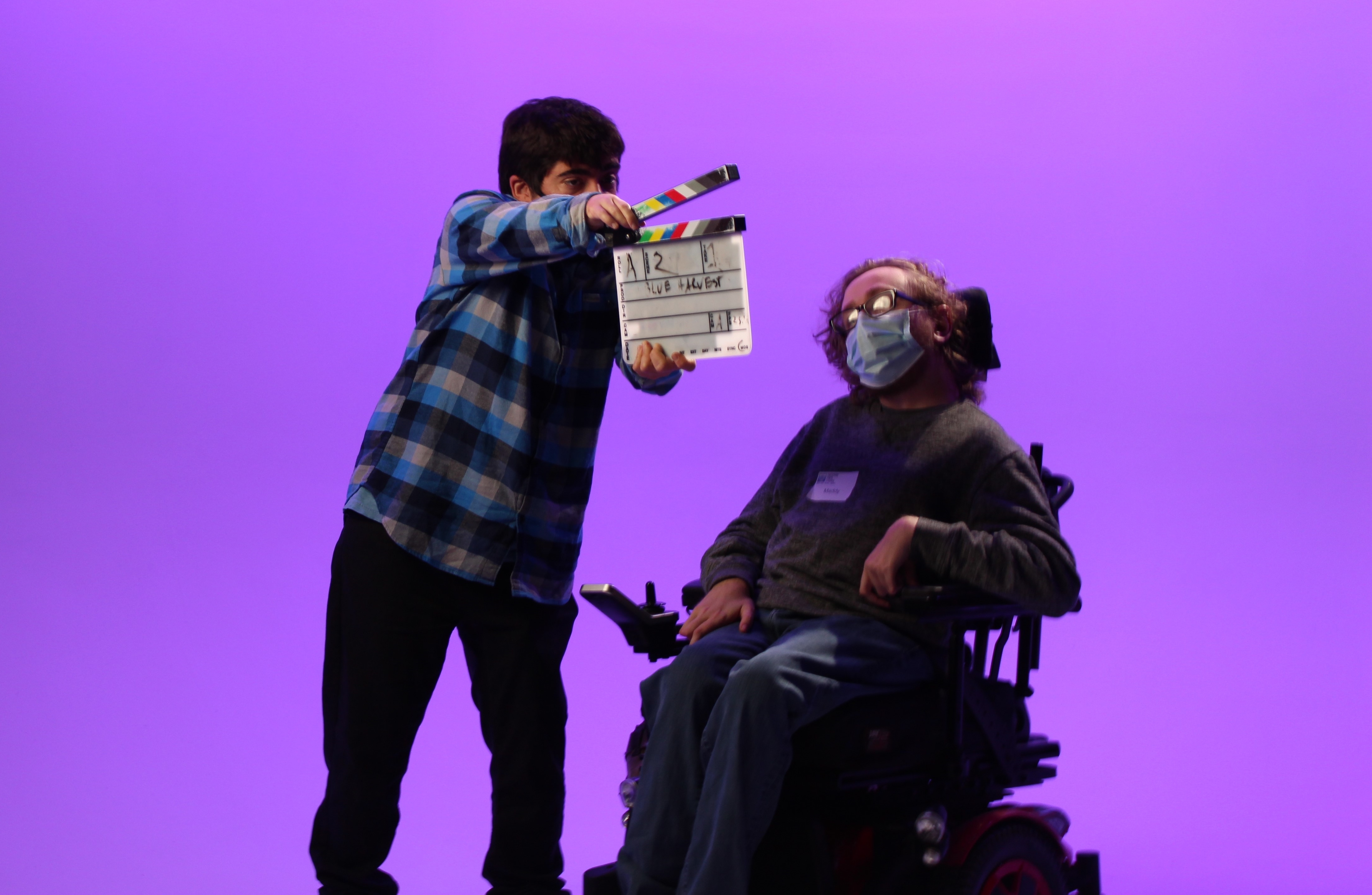 Photo of a man snapping a clapperboard in front of man in to indicate filming has begun.