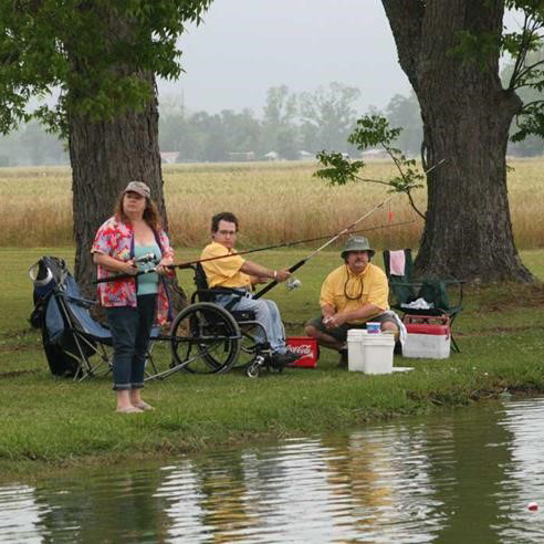 Three people, one in a wheelchair, fishing on river bank