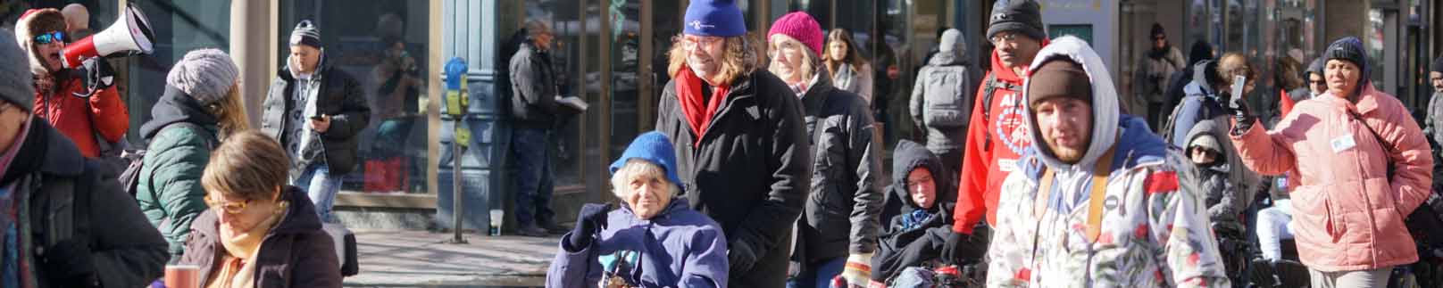 People with and without disabilities bundled up because of the cold walking along a sidewalk as part of a demonstration.