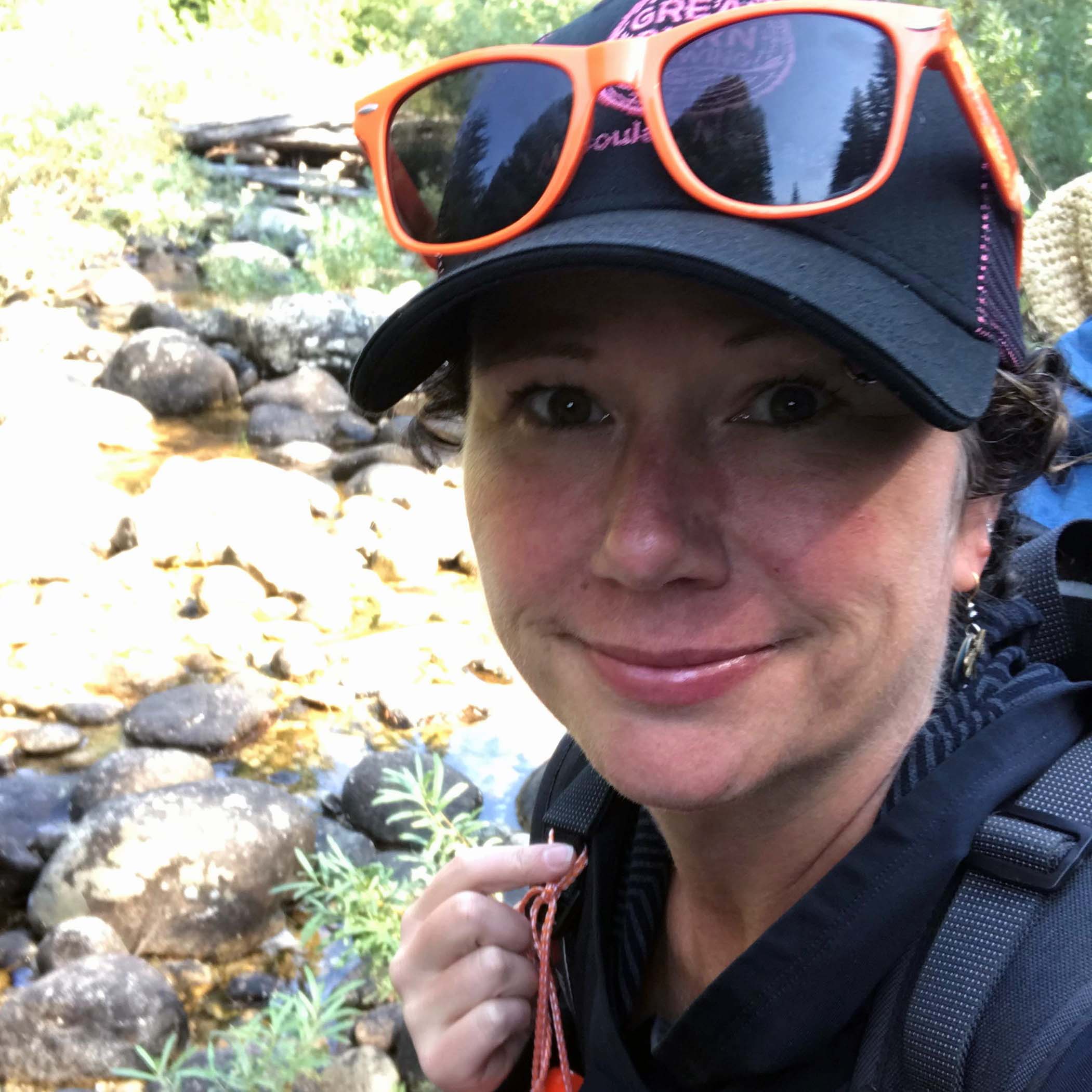 Dr. Rayna Sage, a woman wearing a ball cap on a hike in the woods