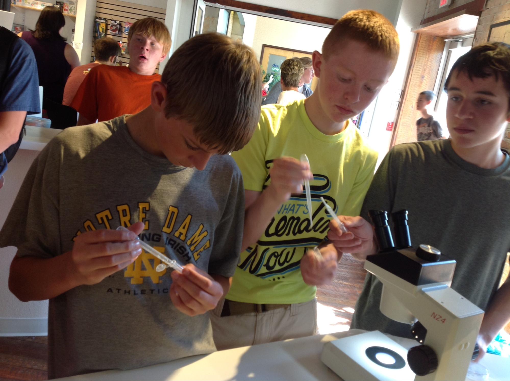 3 boys holding pipets in front of a microscope