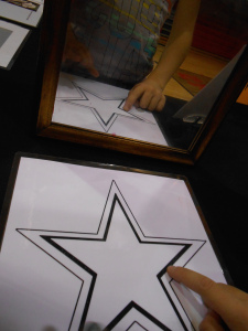A small scientist trying to keep her finger between the two lines of the star as she traces it while only looking at the reflection in the mirror.
