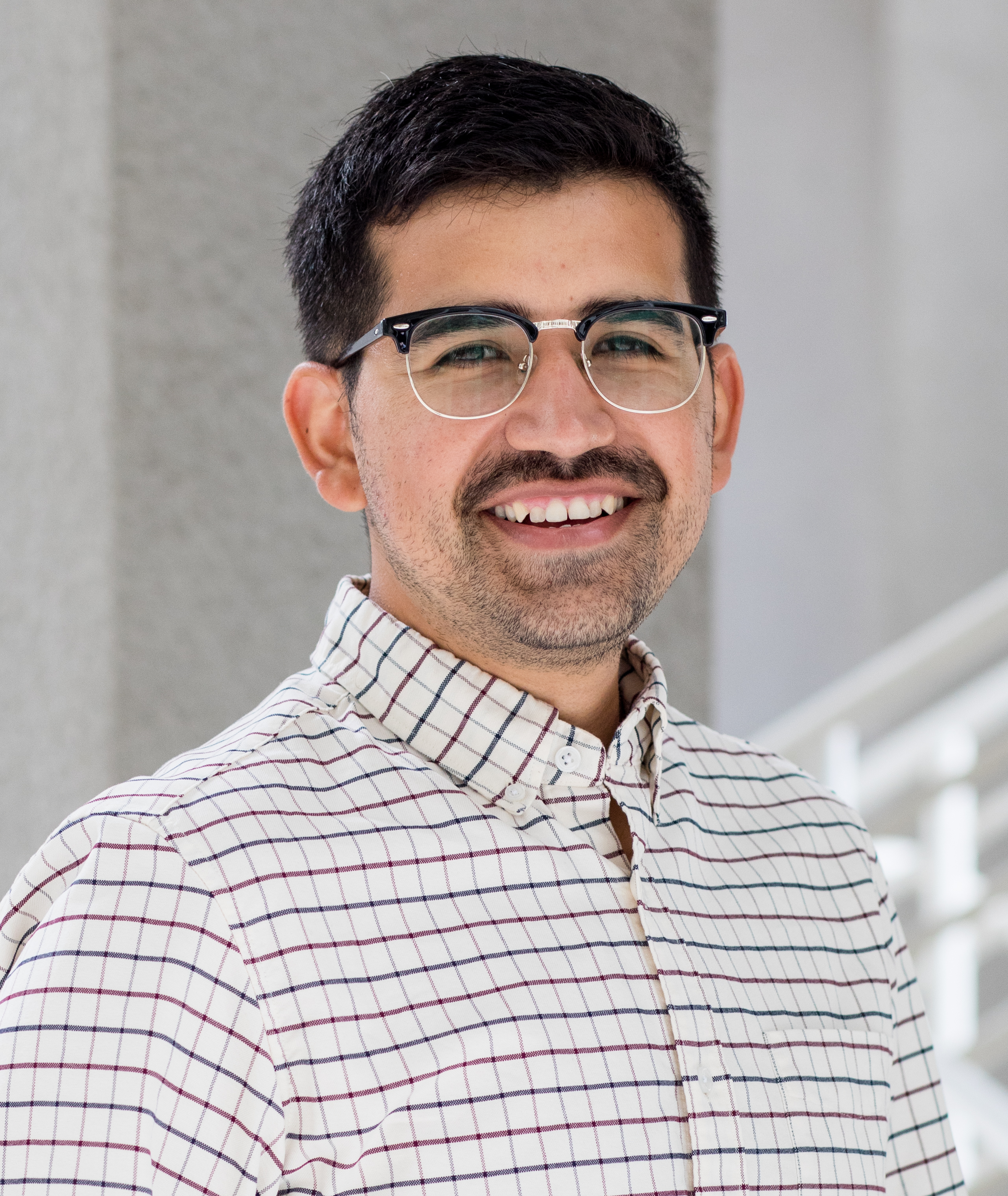 person in maroon grey and white checkered shirt with black upper rim glasses
