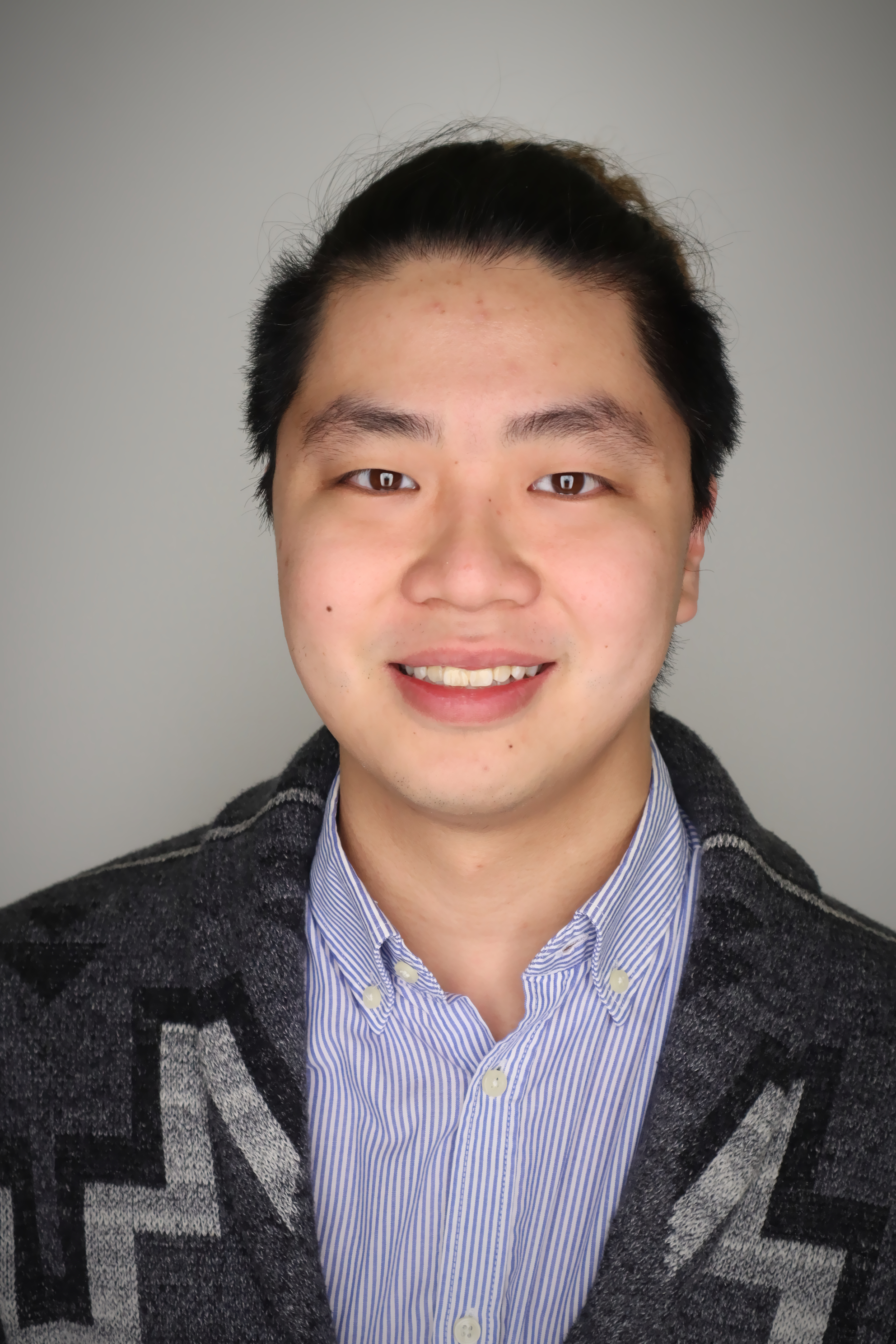 person in a grey and black pattern sweater with blue striped shirt with grey background