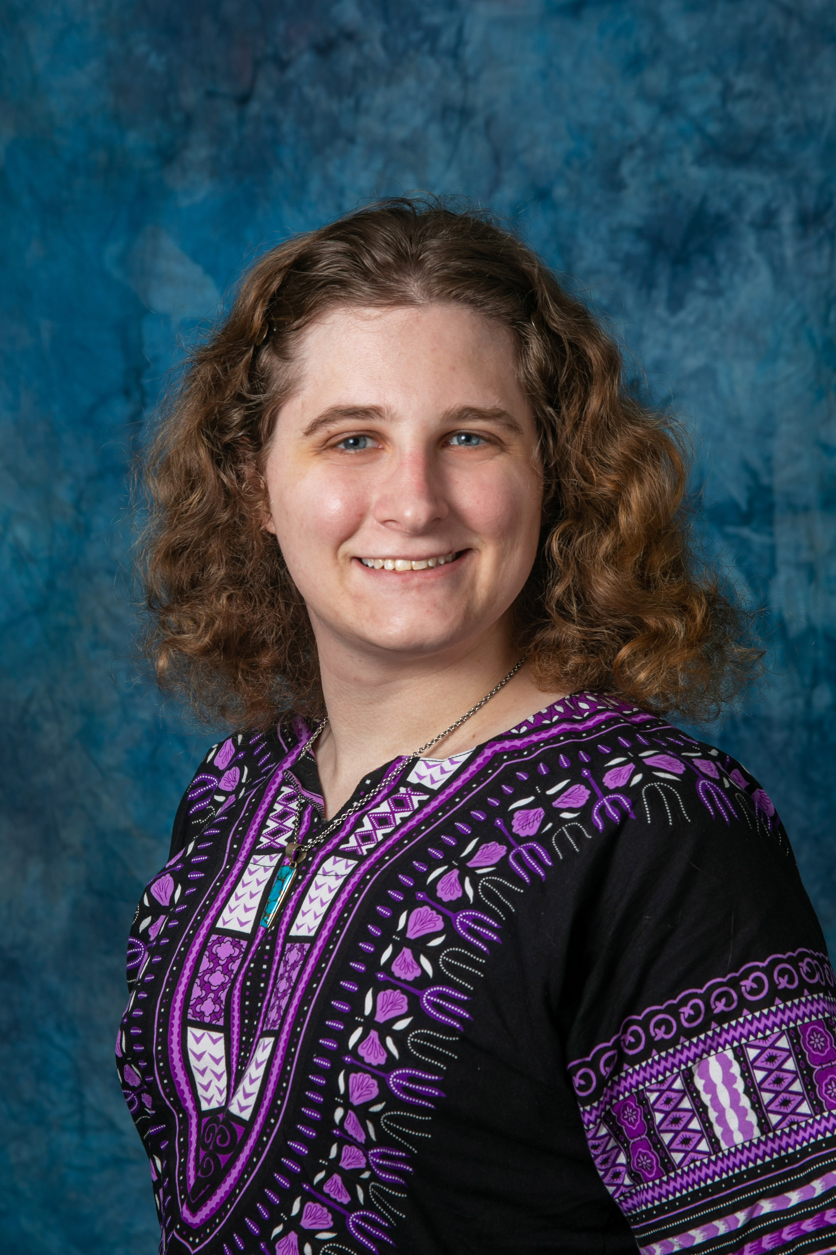 person in purlplem grey, white top with reddish brown wavy hair.