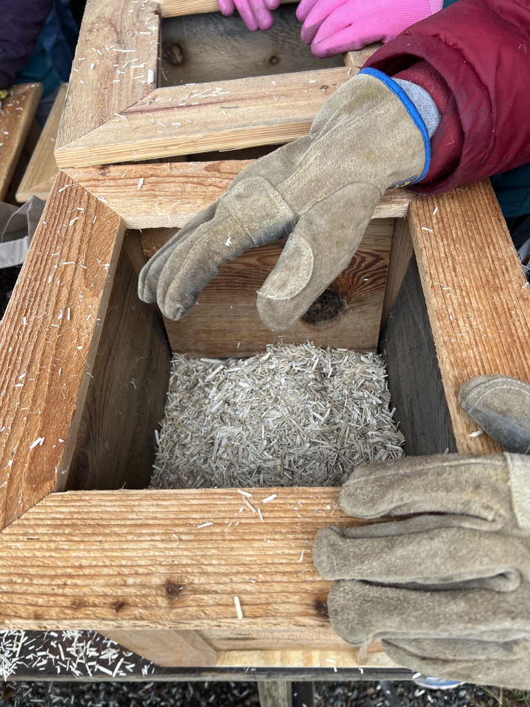 gloved hands putting sticks and twigs into garden boxes