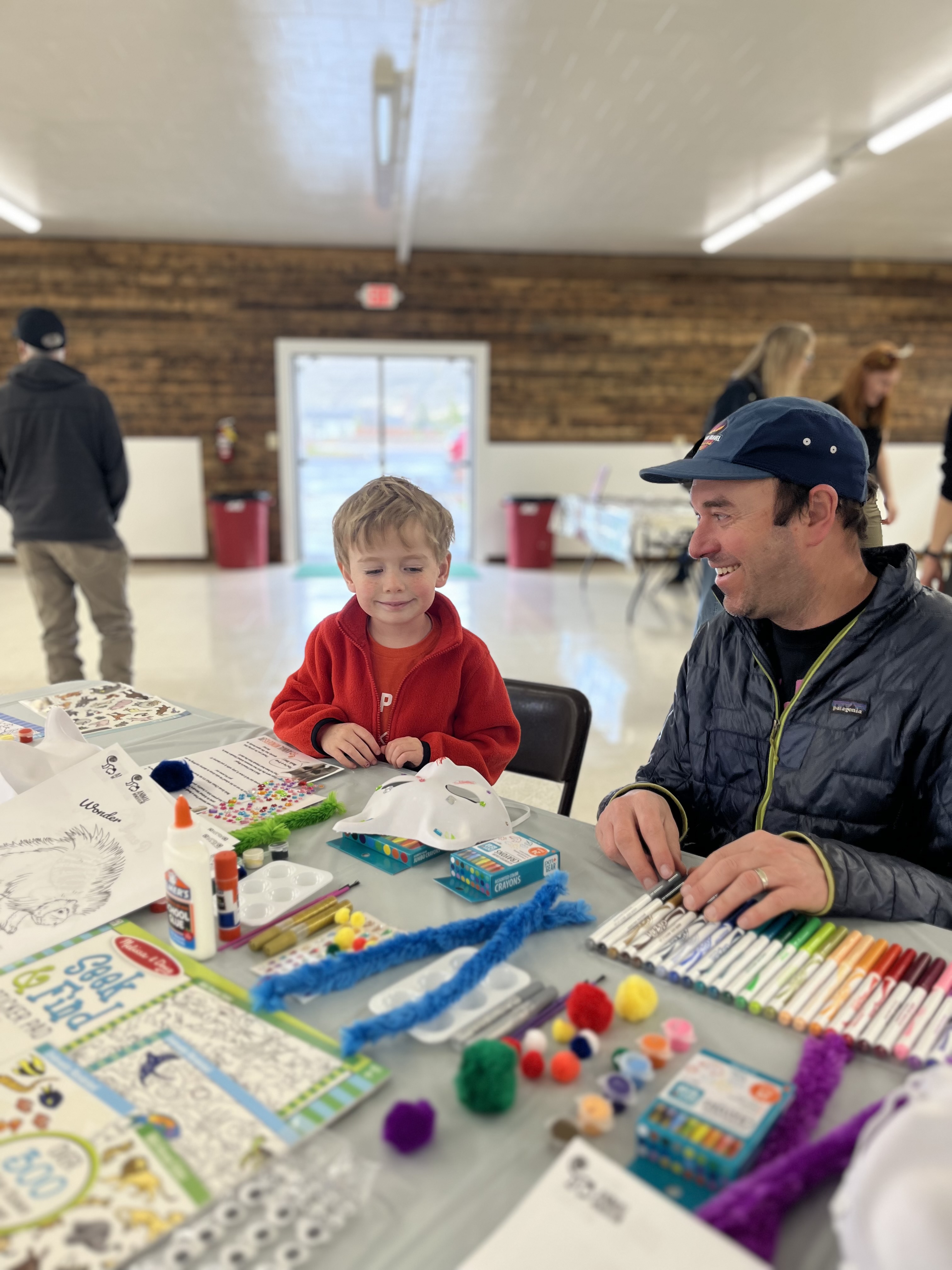 A father and son decorate a raccoon mask. 