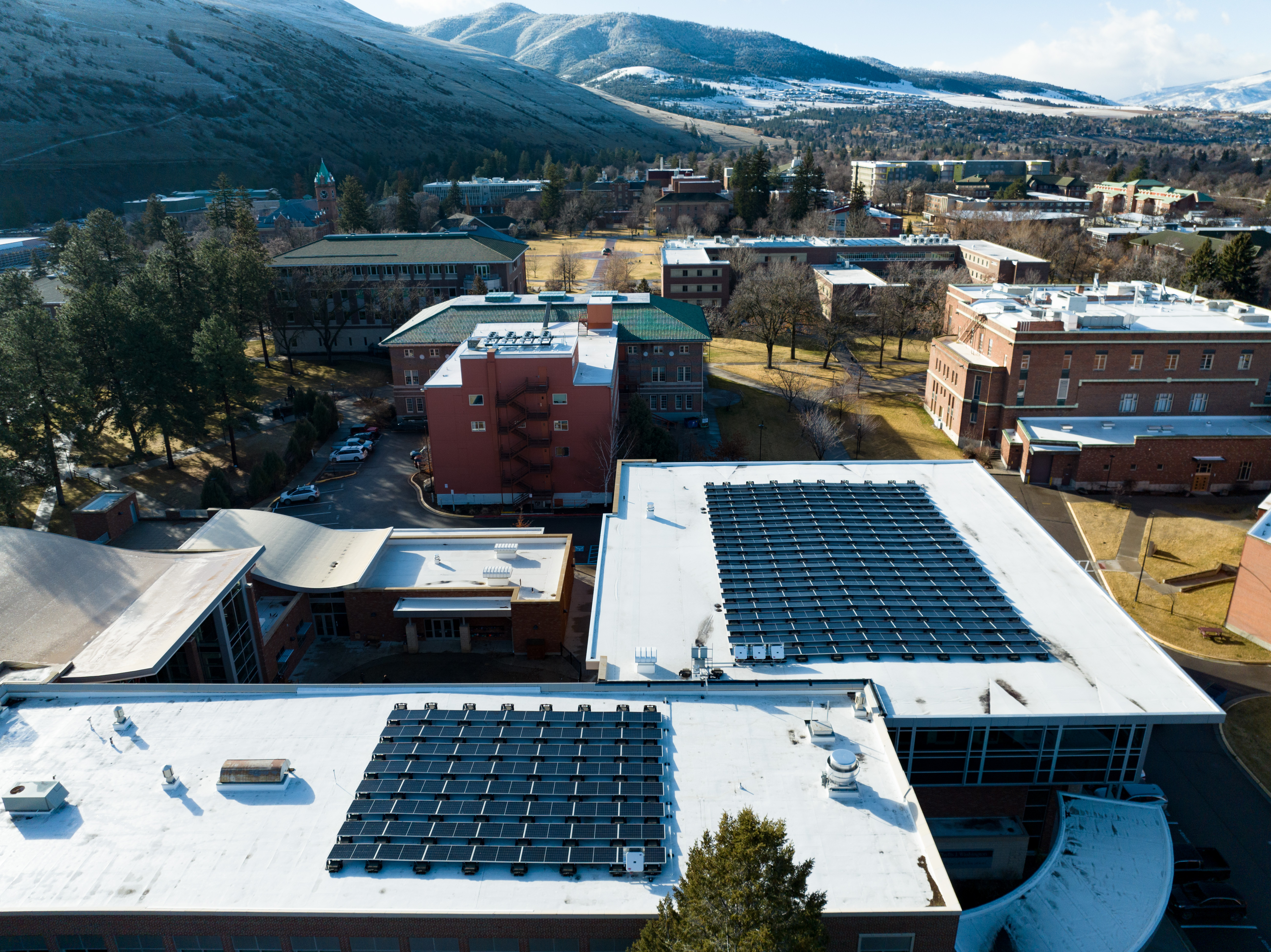 Aerial view of a campus with rooftop solar panels on white buildings, set against snow-dusted mountains in the background.