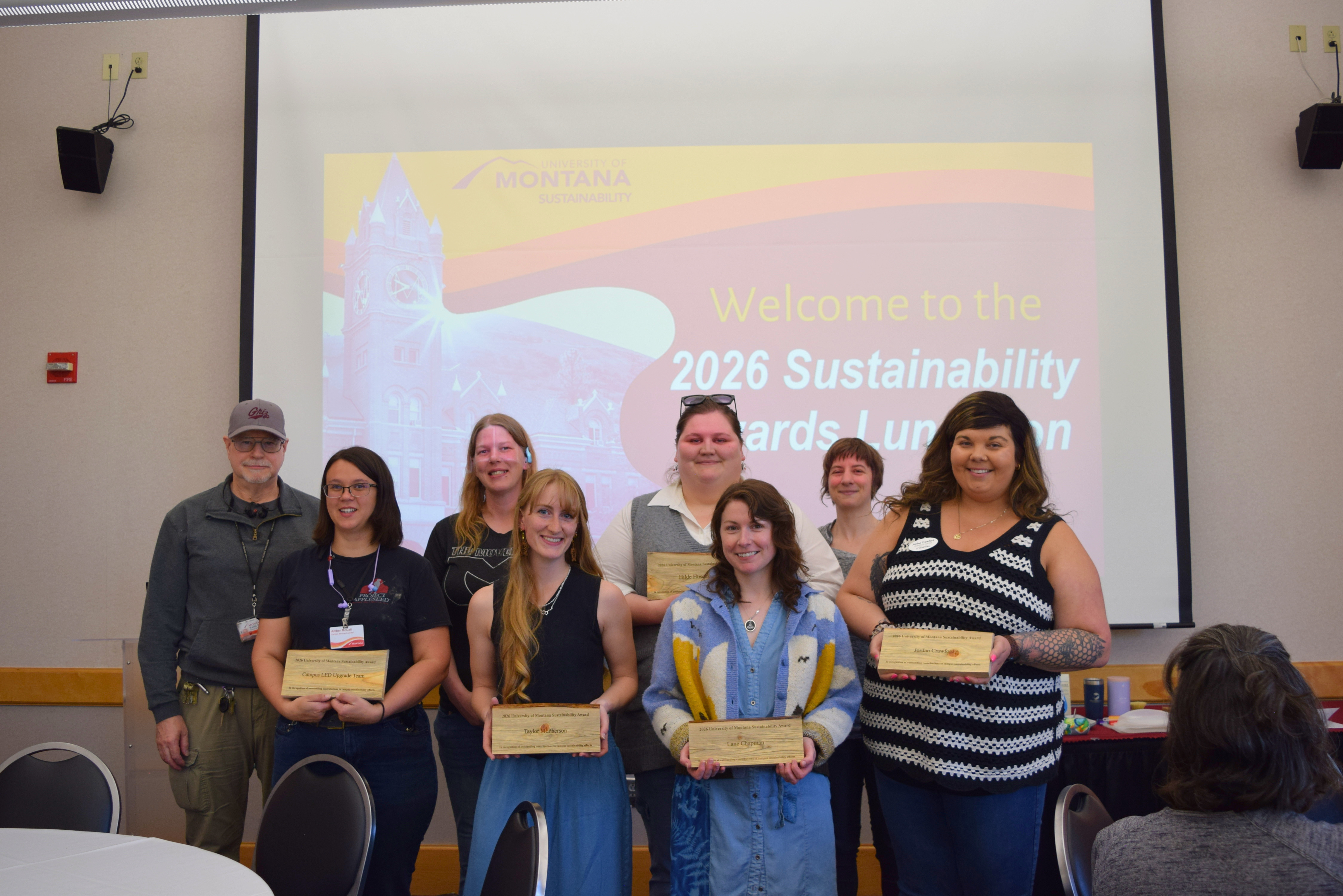 Group of award recipients posing with plaques in front of a projected “2026 Sustainability Awards Luncheon” slide.