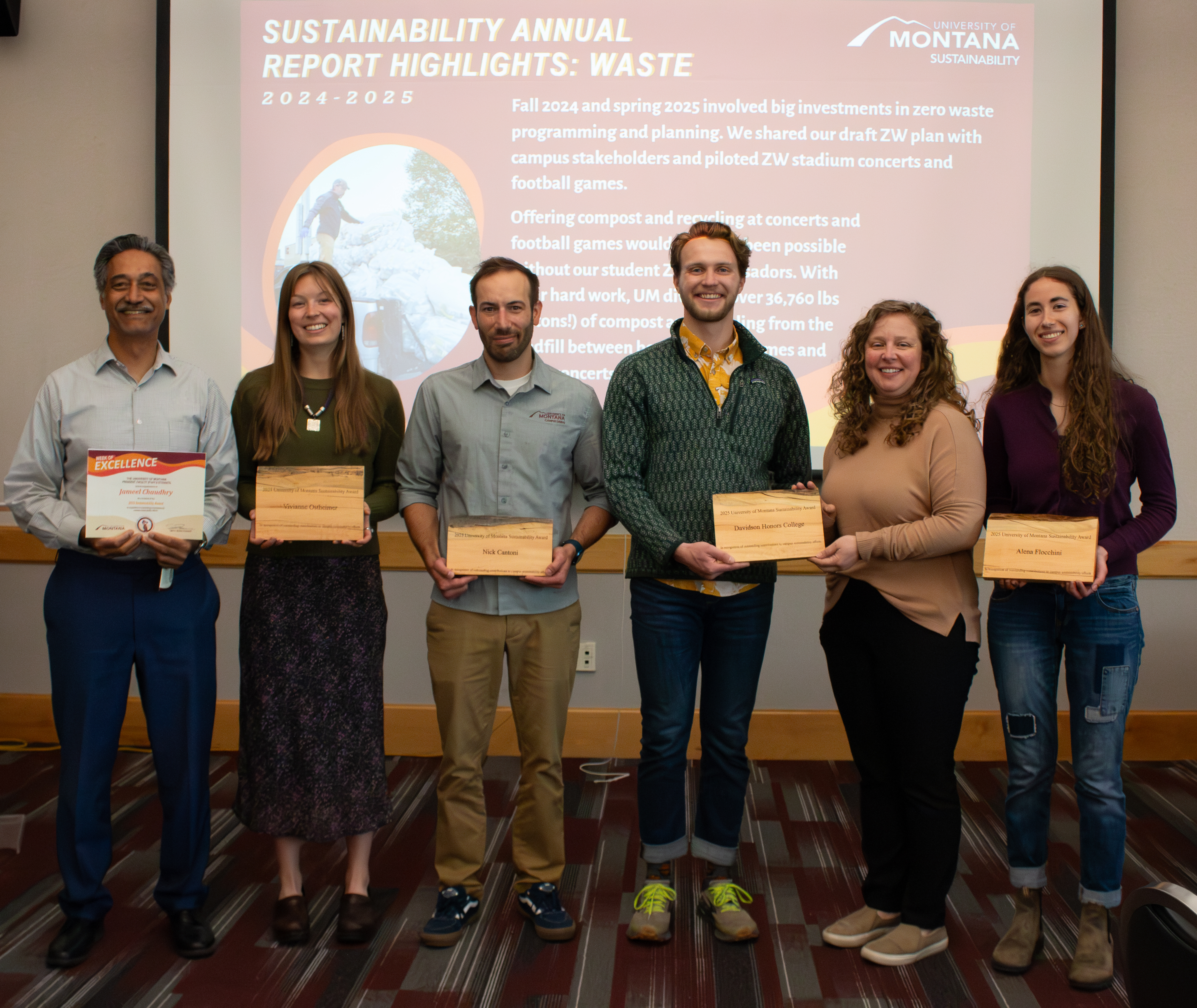all award winners pose in front of a room, in front of a projector, with their wooden sustainability awards