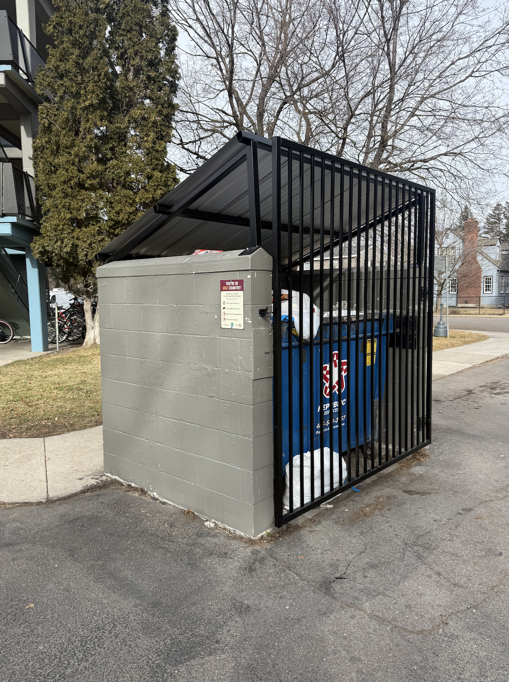 blue dumpster enclosed by concrete and metal gate to prevent bears from eating trash