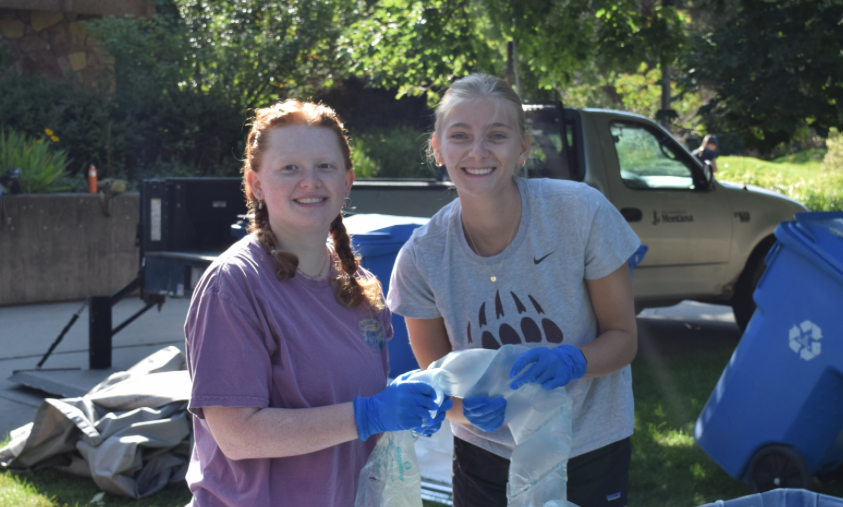 two girls smiling with latex gloves on sorting trash.