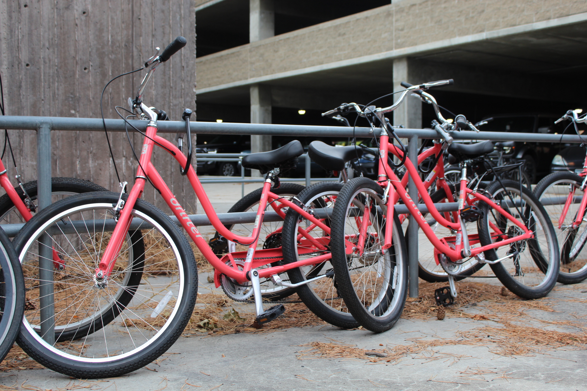 Red bicycles parked at a bike rack outside a parking garage.