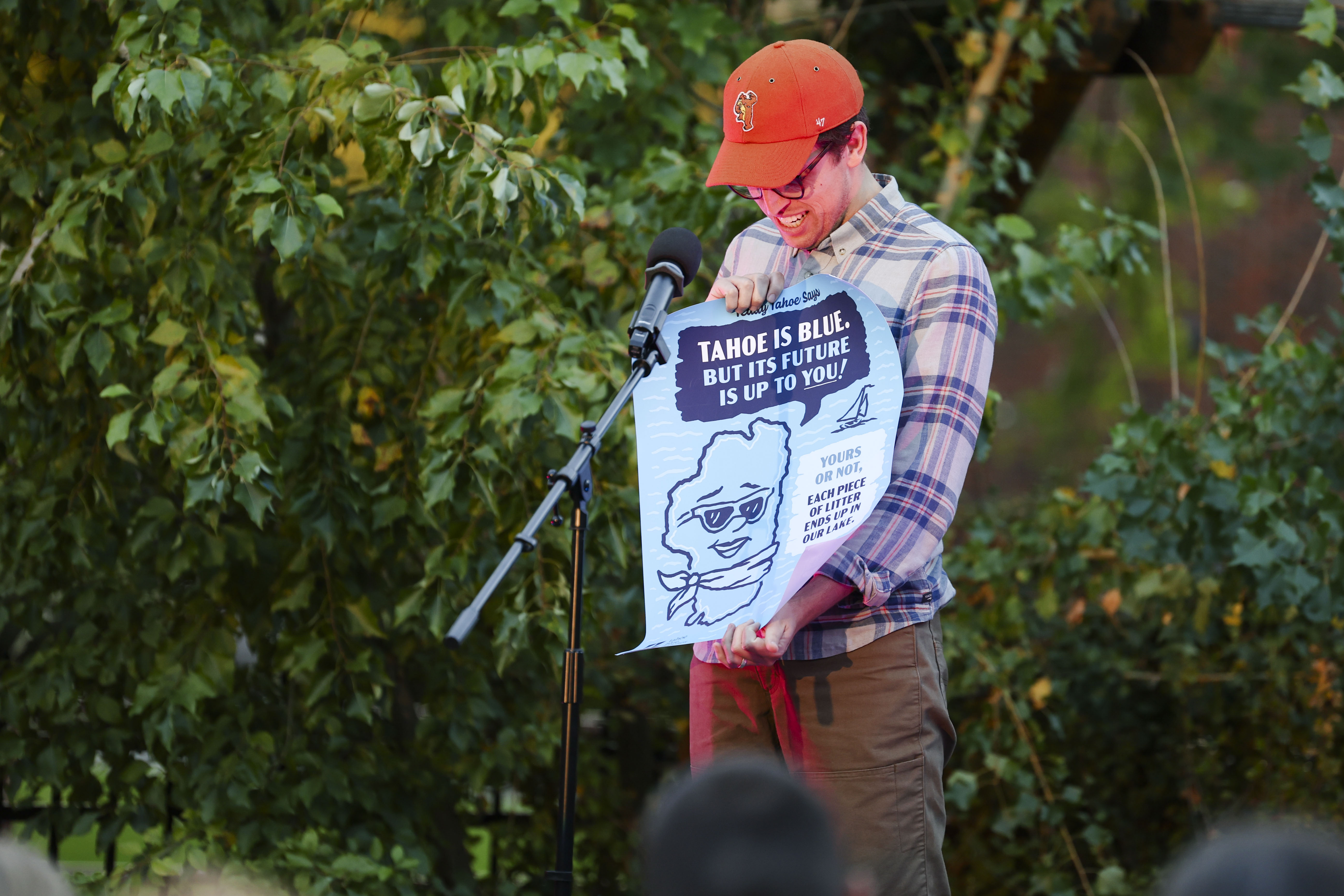Person standing at a microphone holding a poster that reads, “Tahoe is blue, but its future is up to you!”.