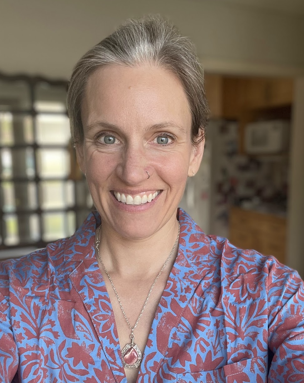 Smiling woman with short brown hair wearing a colorful patterned shirt and necklace.