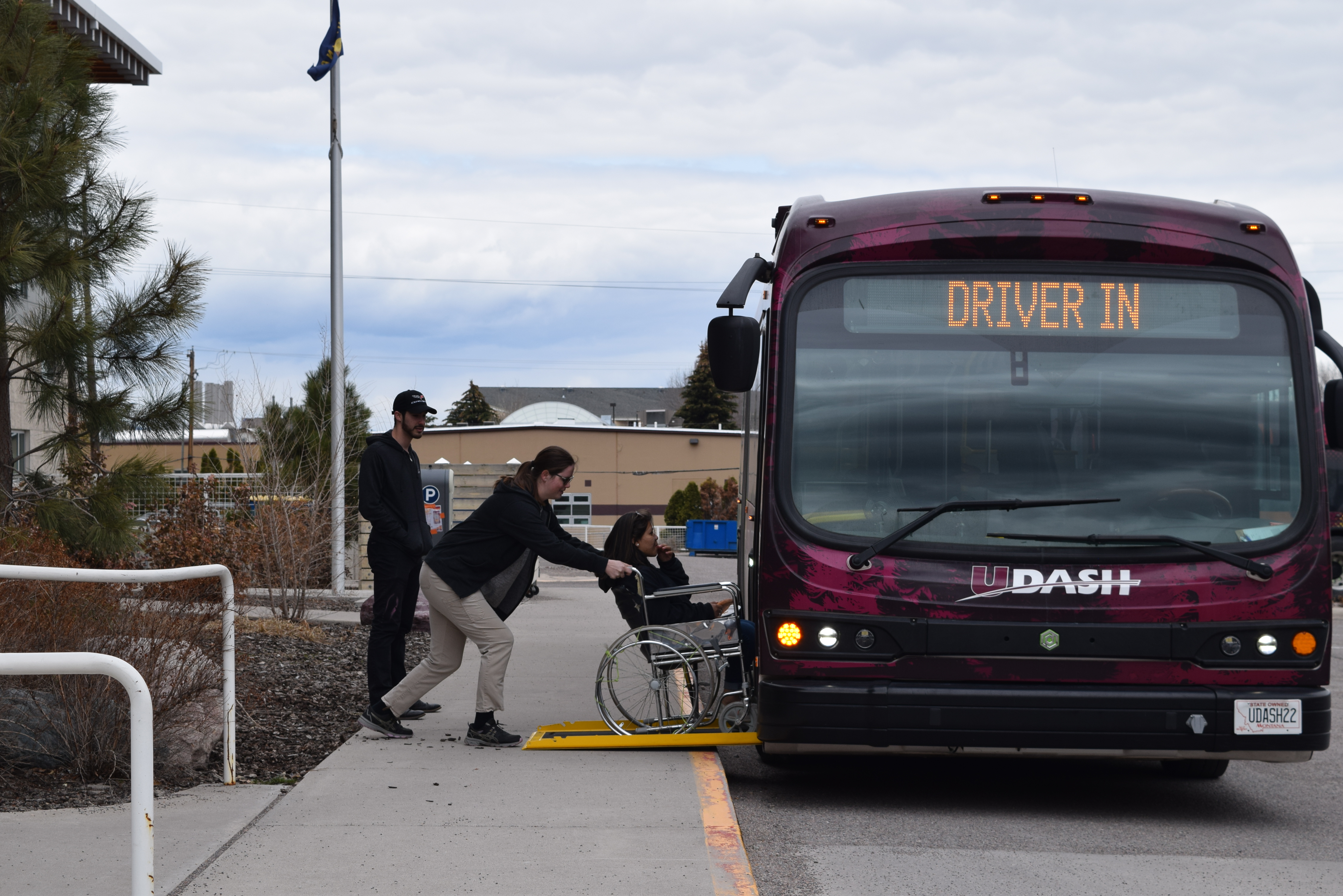A driver pushing a woman in wheelchair up onto the ramp on the bus