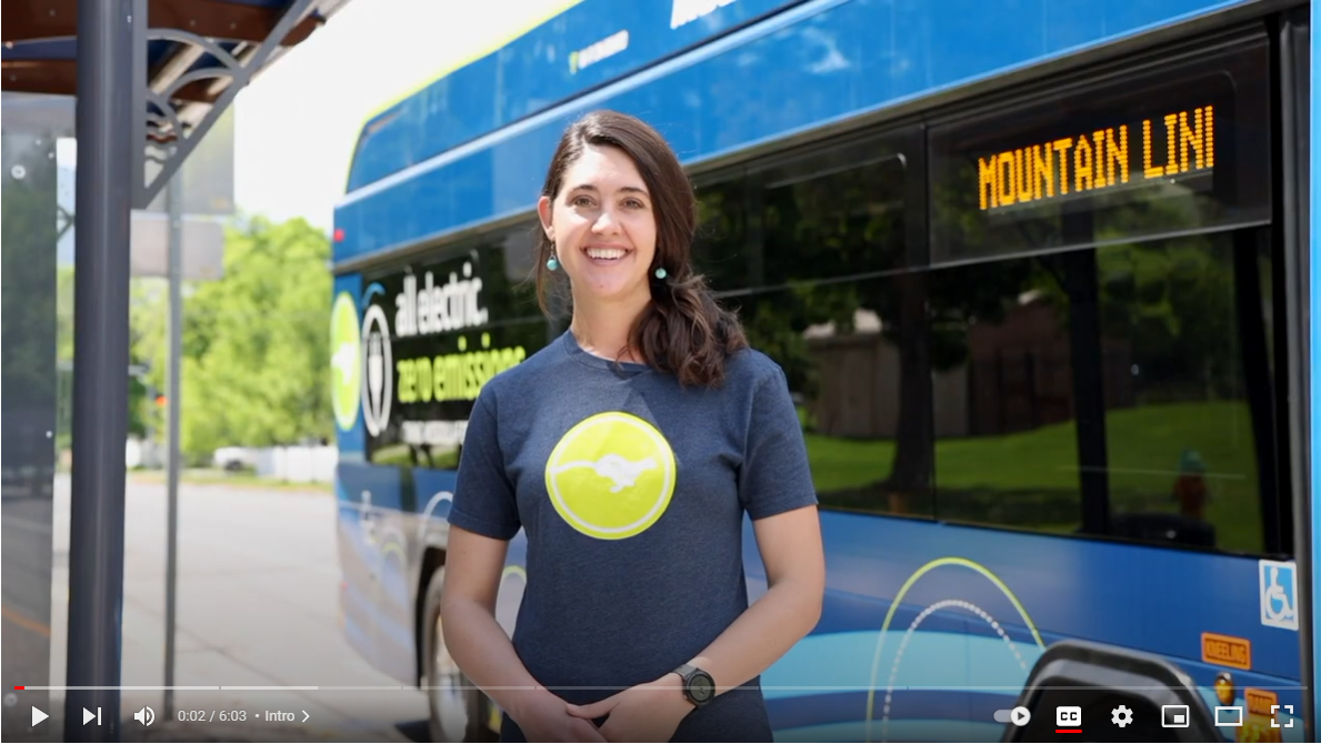 screenshot of Mountain Line Video from Youtube, person is smiling while standing in front of the bus