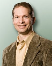 Smiling brian pangrle in a brown blazer and light shirt against a light green background.