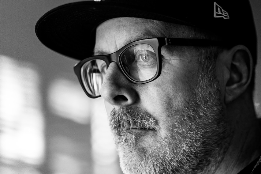 Black-and-white close-up portrait of Jeremy Sauter wearing glasses and a baseball cap, looking thoughtfully into the distance.