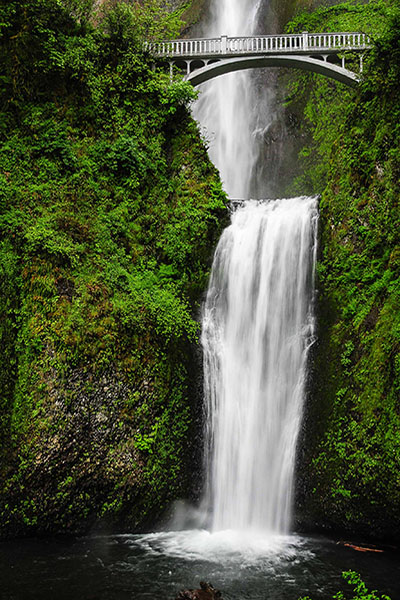 water going down green cliffs with bridge in the background