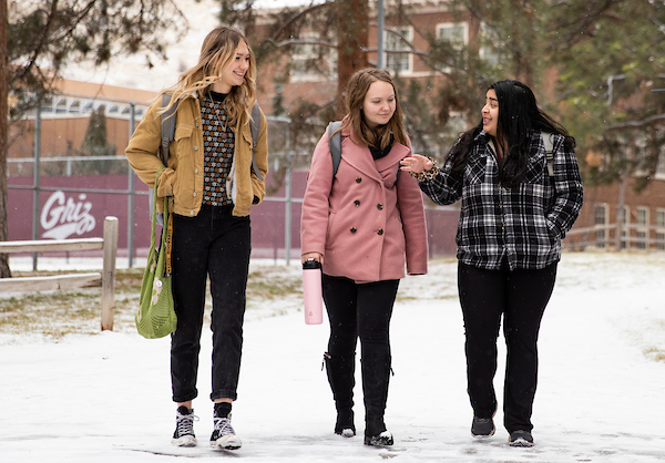 three women walk on campus