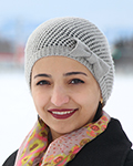 Smiling Amal Al-Misbahi wearing a knit beanie and patterned scarf outdoors in winter.