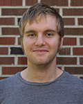 Portrait of Brian Wemple man in a gray shirt standing in front of a brick wall.