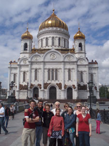 Group of people posing in front of the Cathedral of Christ the Saviour with gold domes under a cloudy sky.